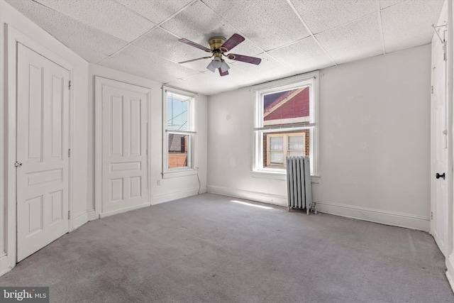 unfurnished bedroom with a ceiling fan, a paneled ceiling, baseboards, carpet floors, and radiator