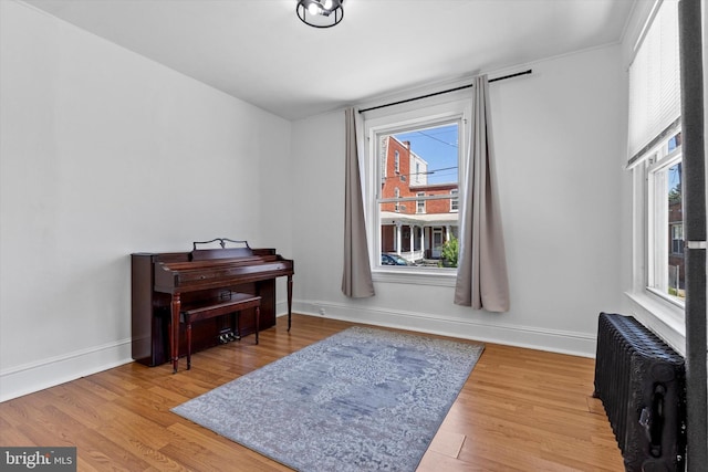 living area with baseboards, a healthy amount of sunlight, radiator heating unit, and wood finished floors