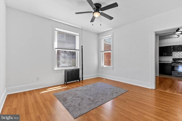 unfurnished room with baseboards, ceiling fan, radiator heating unit, and wood finished floors