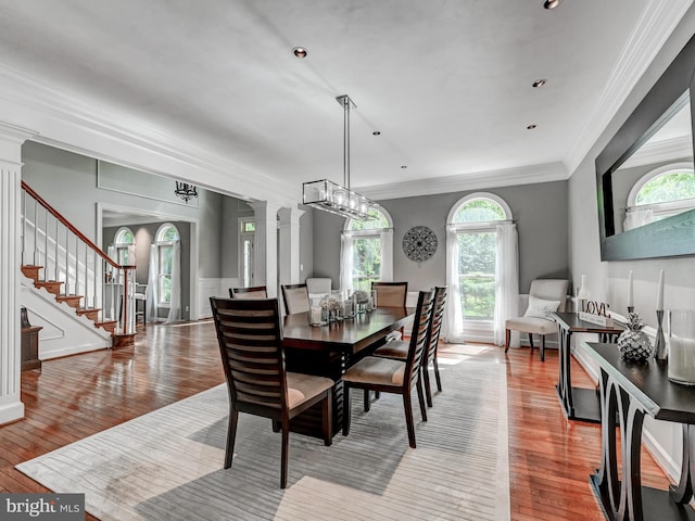 dining room featuring ornate columns, hardwood / wood-style flooring, crown molding, and stairs
