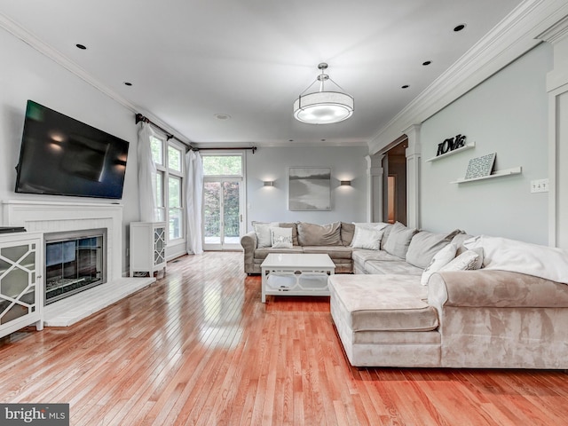 living room with light wood-style floors, crown molding, a glass covered fireplace, and decorative columns