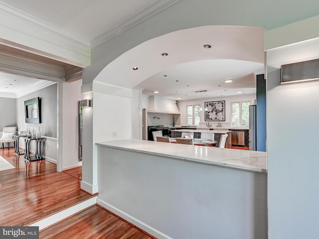 kitchen featuring premium range hood, crown molding, wood finished floors, light stone counters, and a peninsula