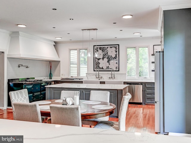 kitchen with stainless steel appliances, custom exhaust hood, a center island, light wood-style floors, and ornamental molding