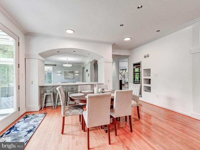 dining area featuring ornamental molding, light wood finished floors, plenty of natural light, arched walkways, and built in shelves