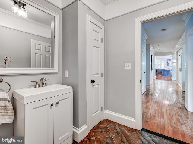 bathroom featuring crown molding, baseboards, vanity, and wood-type flooring
