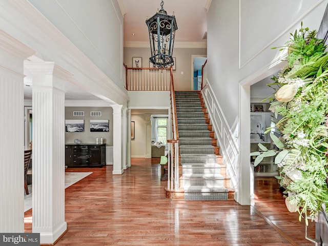 entrance foyer with ornate columns, a towering ceiling, stairs, light wood-style floors, and crown molding
