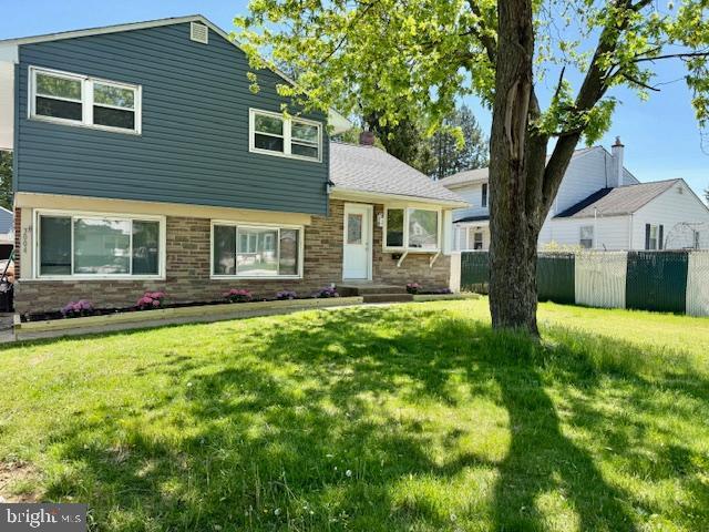 split level home featuring fence, a front yard, and stone siding