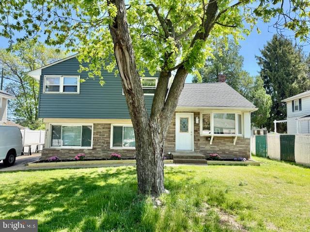 split level home with brick siding, fence, entry steps, and a front lawn