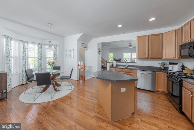 kitchen featuring a kitchen island, dark countertops, a sink, black appliances, and light wood-style flooring
