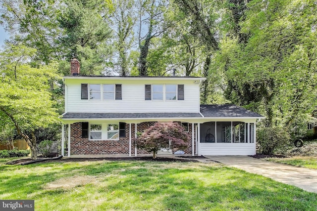 traditional-style house featuring a sunroom, roof with shingles, a front yard, and a chimney