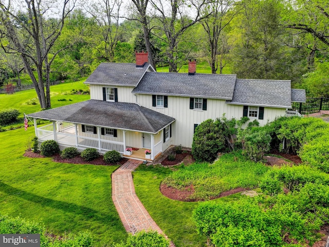 view of front of property with covered porch, a chimney, a front yard, a shingled roof, and board and batten siding