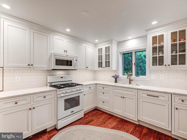 kitchen with white appliances, a sink, white cabinets, wood finished floors, and recessed lighting