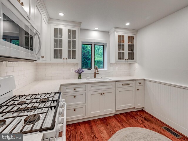 kitchen with white microwave, gas range oven, a sink, wood finished floors, and a wainscoted wall