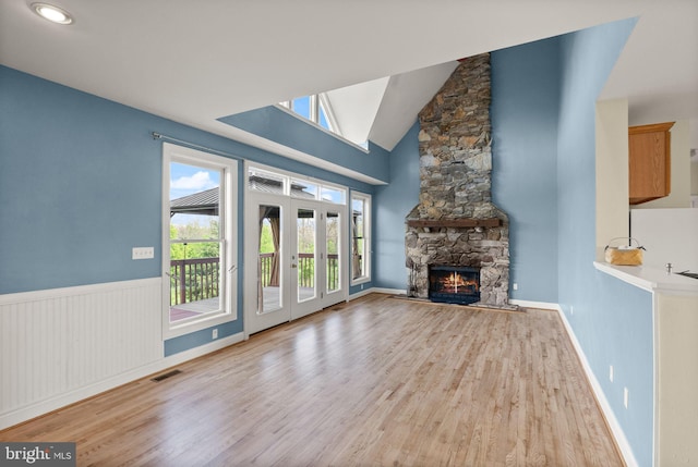 unfurnished living room featuring high vaulted ceiling, visible vents, a stone fireplace, and wood finished floors