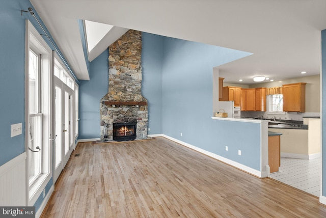 unfurnished living room featuring light wood-style floors, baseboards, vaulted ceiling, and a stone fireplace