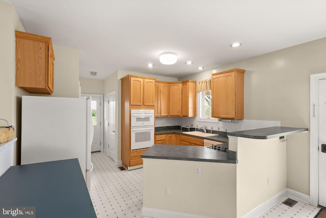 kitchen featuring white appliances, a peninsula, baseboards, and a sink