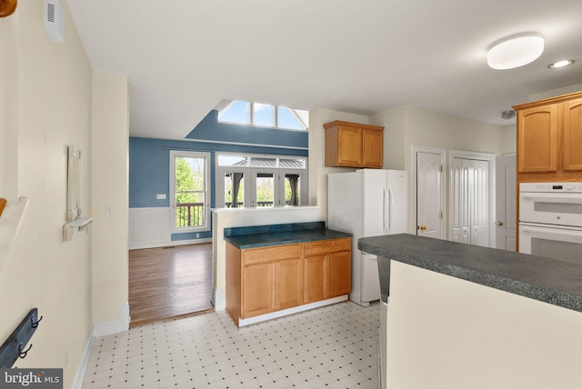 kitchen featuring white appliances, dark countertops, baseboards, and light floors
