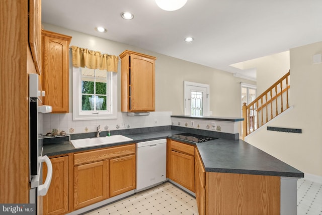 kitchen with white dishwasher, dark countertops, tasteful backsplash, a sink, and a peninsula