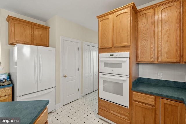 kitchen featuring dark countertops, tasteful backsplash, white appliances, and light floors