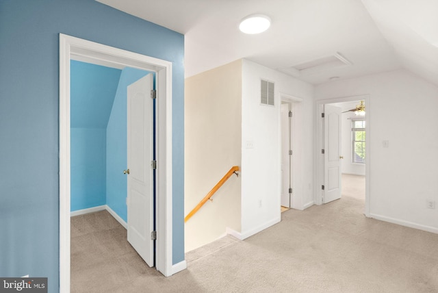 hallway with carpet flooring, visible vents, baseboards, an upstairs landing, and vaulted ceiling