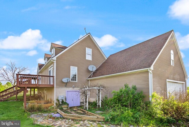 back of property with a garage, a shingled roof, a deck, and stairway