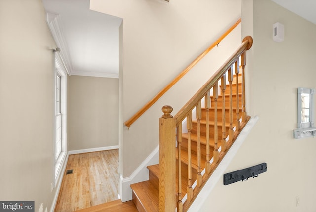 stairway featuring visible vents, baseboards, crown molding, and wood finished floors