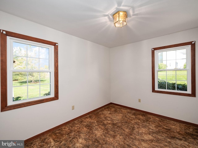 spare room with baseboards, a healthy amount of sunlight, and dark colored carpet