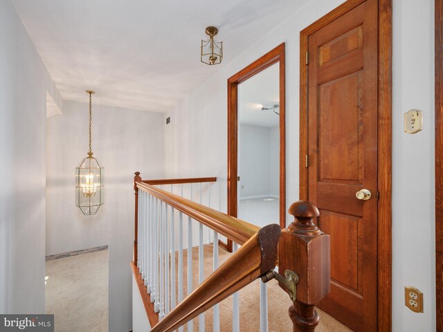 hall featuring carpet flooring, a chandelier, and an upstairs landing