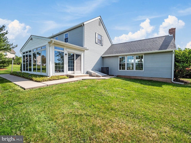 back of house with roof with shingles, a chimney, a sunroom, central AC unit, and a yard