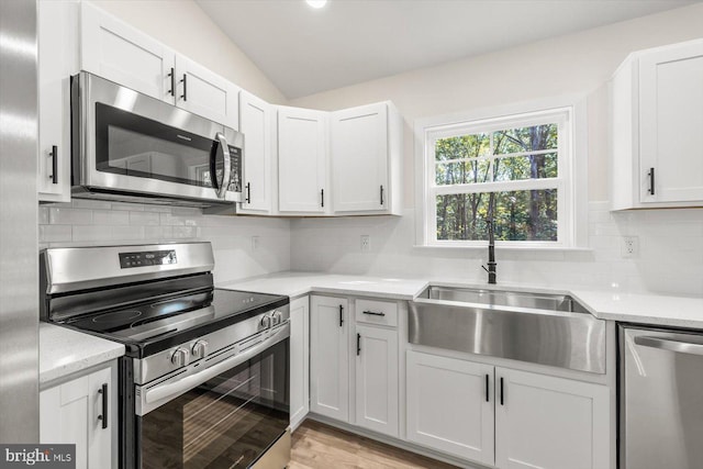 kitchen with appliances with stainless steel finishes, a sink, white cabinetry, backsplash, and vaulted ceiling