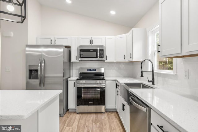 kitchen with lofted ceiling, light stone counters, a sink, appliances with stainless steel finishes, and backsplash