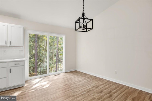 unfurnished dining area featuring an inviting chandelier, baseboards, light wood finished floors, and visible vents