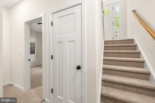 staircase with carpet floors, baseboards, and electric panel