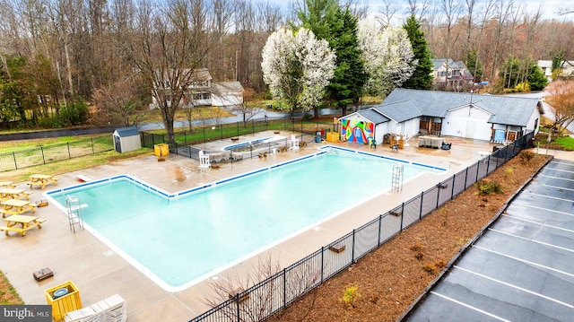 pool with a patio, fence, and an outbuilding