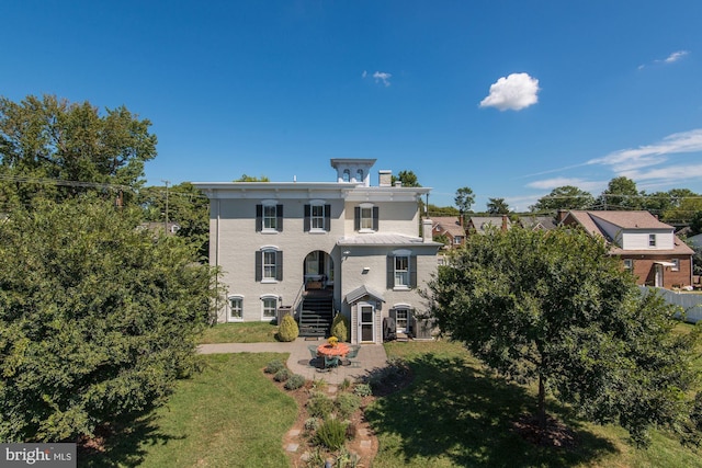 italianate home featuring a patio, a chimney, a front lawn, and stairway