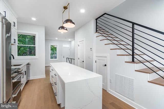 407 16th St SE, Washington, DC 20003 - kitchen featuring light wood-style flooring, white cabinets, decorative light fixtures, a center island, and light stone countertops