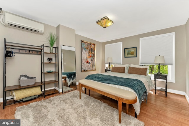 bedroom with baseboards, a wall unit AC, and wood finished floors