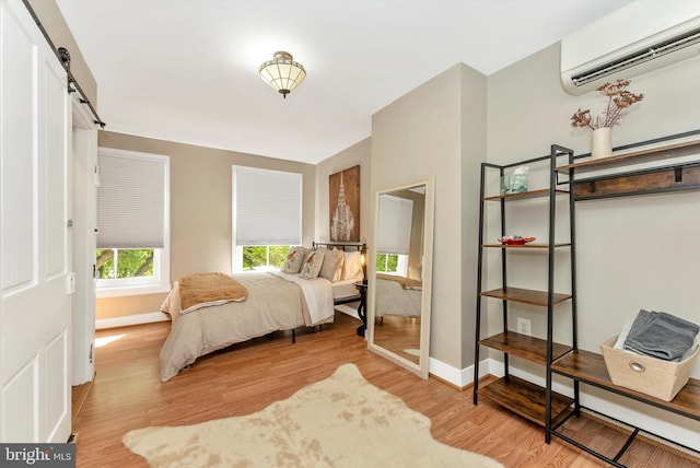 bedroom with a barn door, wood finished floors, baseboards, and a wall mounted AC