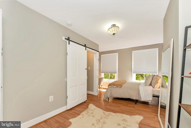 bedroom with baseboards, a barn door, and wood finished floors