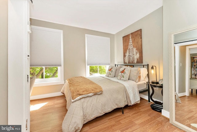 bedroom with baseboards, multiple windows, and light wood-style flooring