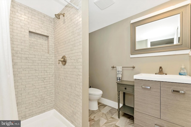bathroom featuring toilet, tiled shower, visible vents, baseboards, and vanity