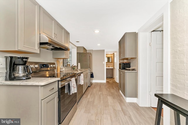kitchen with a sink, gray cabinets, under cabinet range hood, light wood-style flooring, and appliances with stainless steel finishes