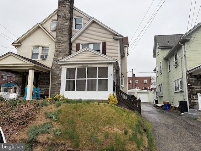 view of front of property featuring a chimney, cooling unit, an outdoor structure, aphalt driveway, and stone siding