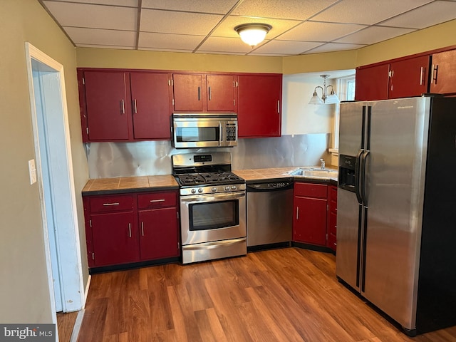 kitchen with stainless steel appliances, a drop ceiling, and red cabinets