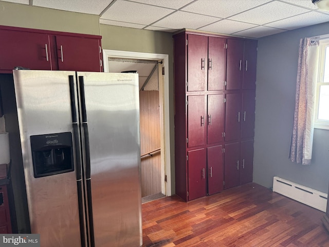 kitchen featuring a paneled ceiling, wood finished floors, a baseboard radiator, stainless steel refrigerator with ice dispenser, and red cabinets