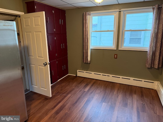 unfurnished room with baseboard heating, a drop ceiling, and dark wood-style floors