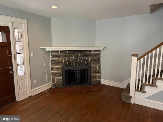unfurnished living room featuring stairs, baseboards, a stone fireplace, and wood finished floors