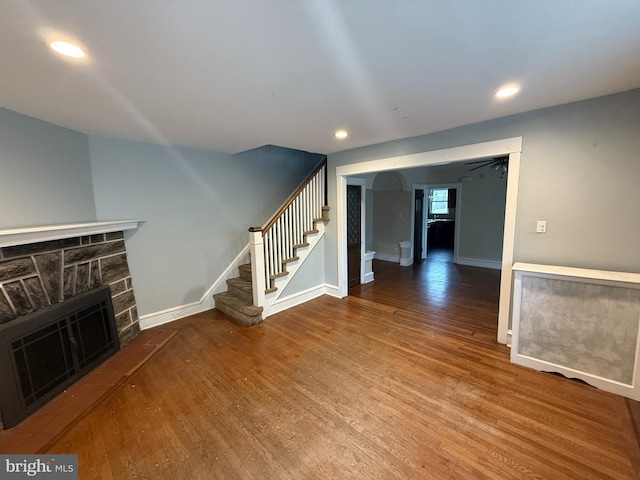 unfurnished living room with stairway, baseboards, a stone fireplace, and wood finished floors