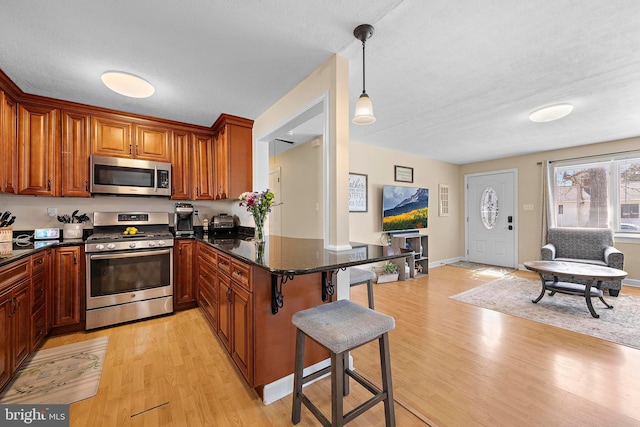 412 Prospect Ave, Pine Beach, NJ 08741 - kitchen featuring brown cabinetry, a kitchen bar, appliances with stainless steel finishes, a peninsula, and light wood-style flooring