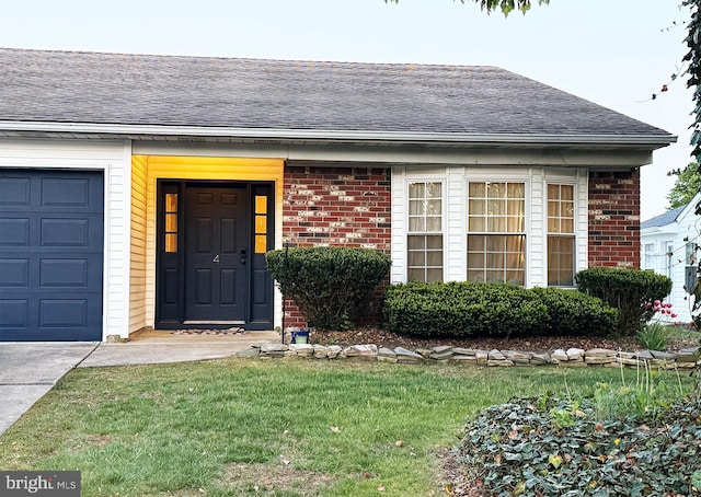 entrance to property with brick siding, a shingled roof, an attached garage, and a yard